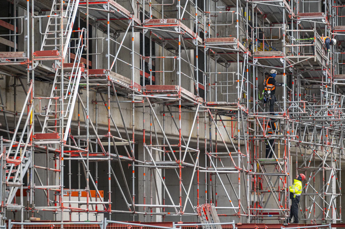 Échafaudage à plusieurs niveaux monté le long d’une façade d’immeuble, ouvriers casqués sur les planchers